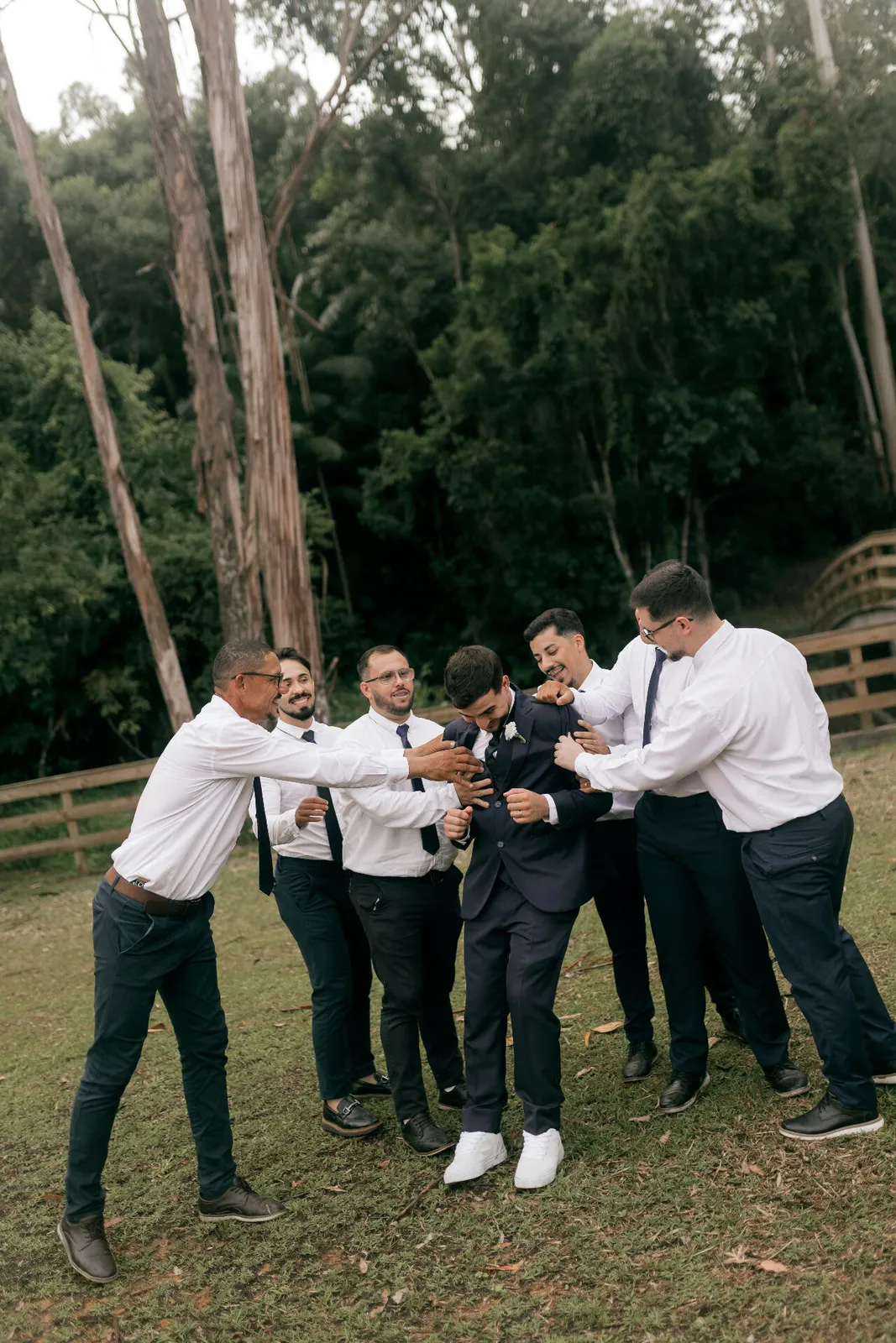 Groomsmen helping the groom adjust his suit jacket together in a forest clearing