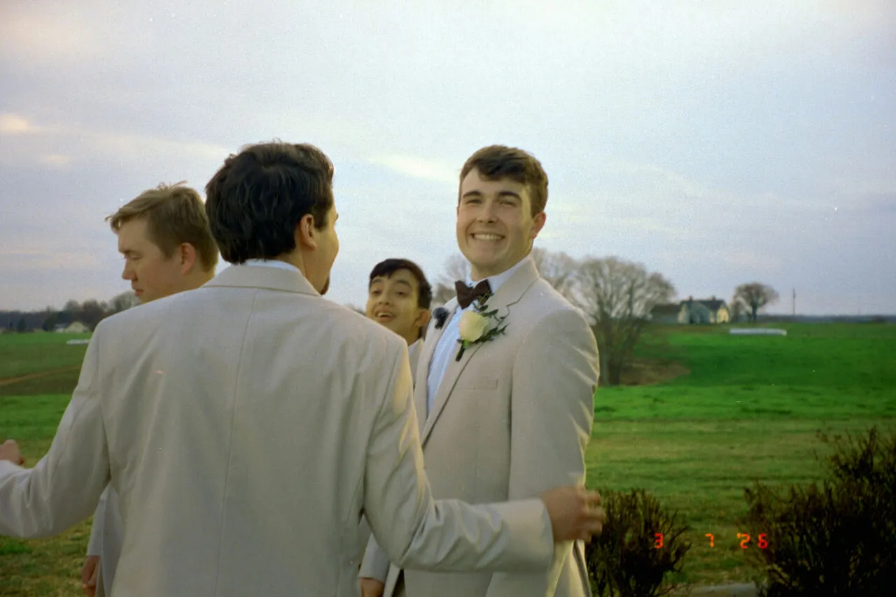 Groomsmen in cream suits laughing together with the groom in a sunlit field