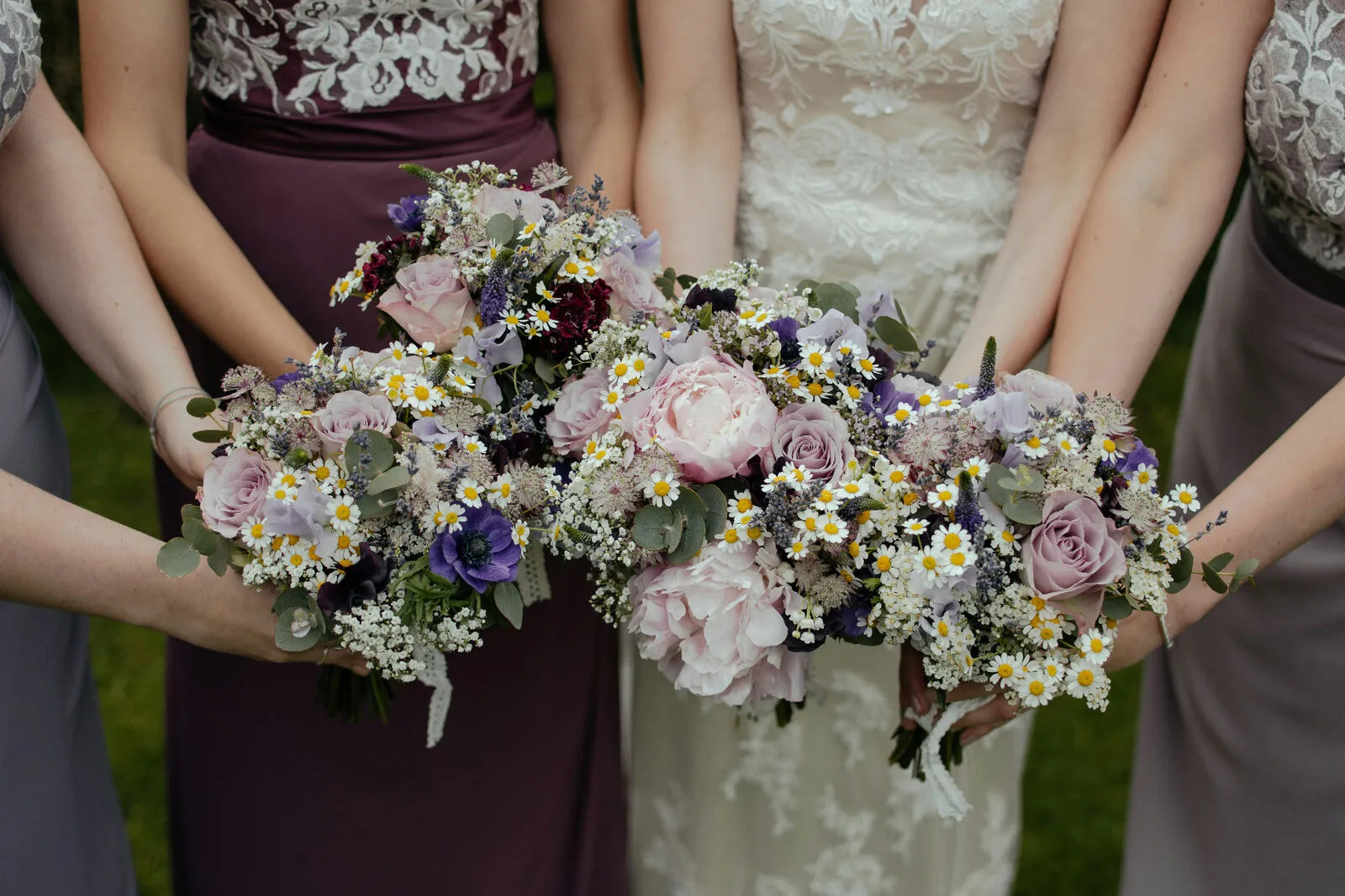 Bride and bridesmaids holding lush pastel bouquets of pink roses, peonies, and wildflowers together