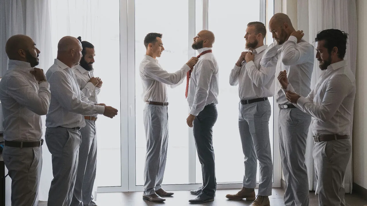 Groomsmen helping the groom adjust his tie before the wedding ceremony