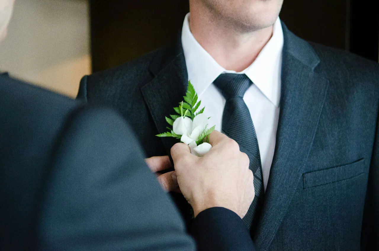 Father pinning a white floral boutonniere onto the groom's lapel before the wedding