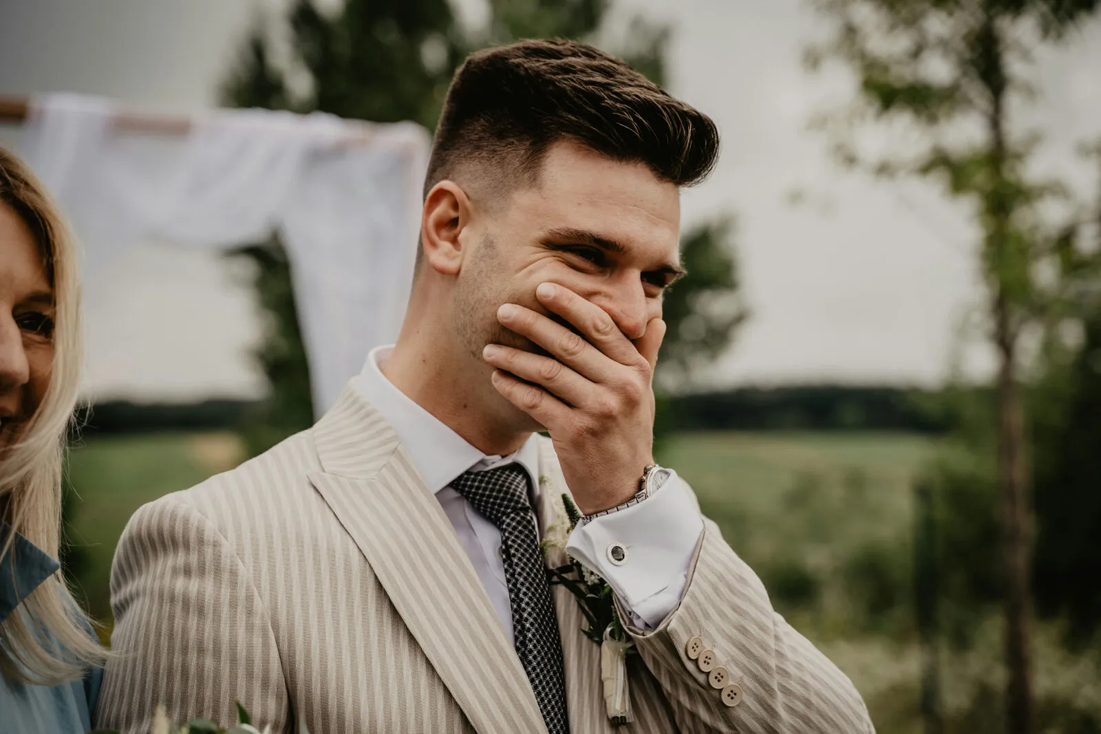 Emotional groom covering his mouth in a moment of joy during an outdoor wedding ceremony