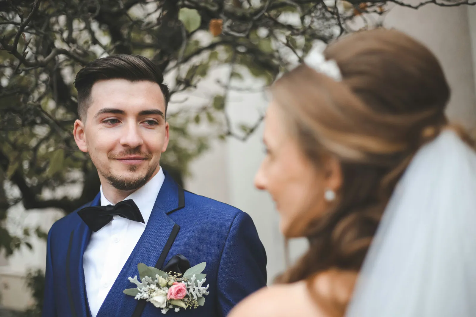 Groom in a blue suit with floral boutonniere looking warmly at his bride during an outdoor wedding