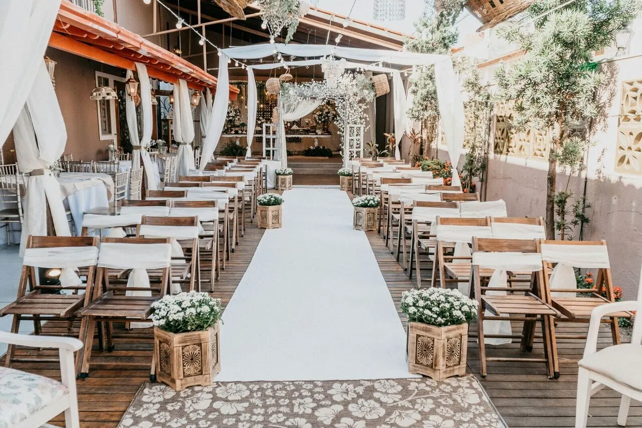 Elegant outdoor wedding ceremony aisle with white drapery, wooden chairs, and floral arrangements