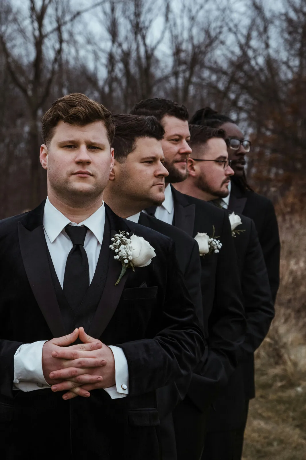 Groom and groomsmen in black tuxedos standing together with white rose boutonnieres before the ceremony