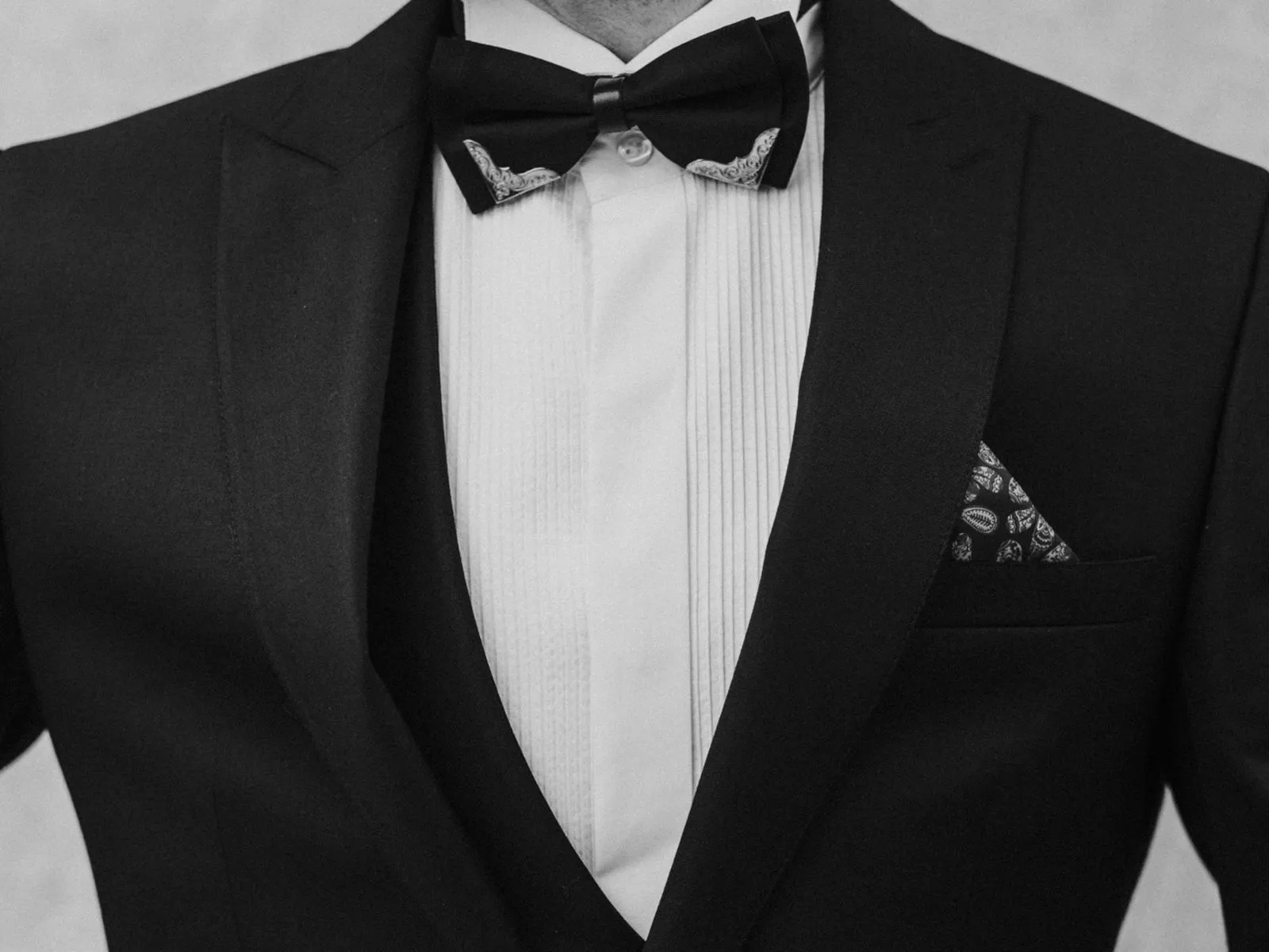 Black and white close-up of a groom in a tuxedo with a bow tie and patterned pocket square