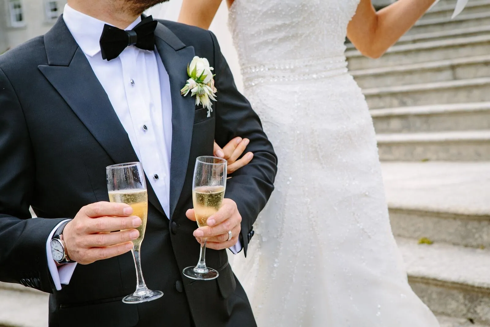 Bride and groom in formal wedding attire holding champagne glasses on the steps after their ceremony