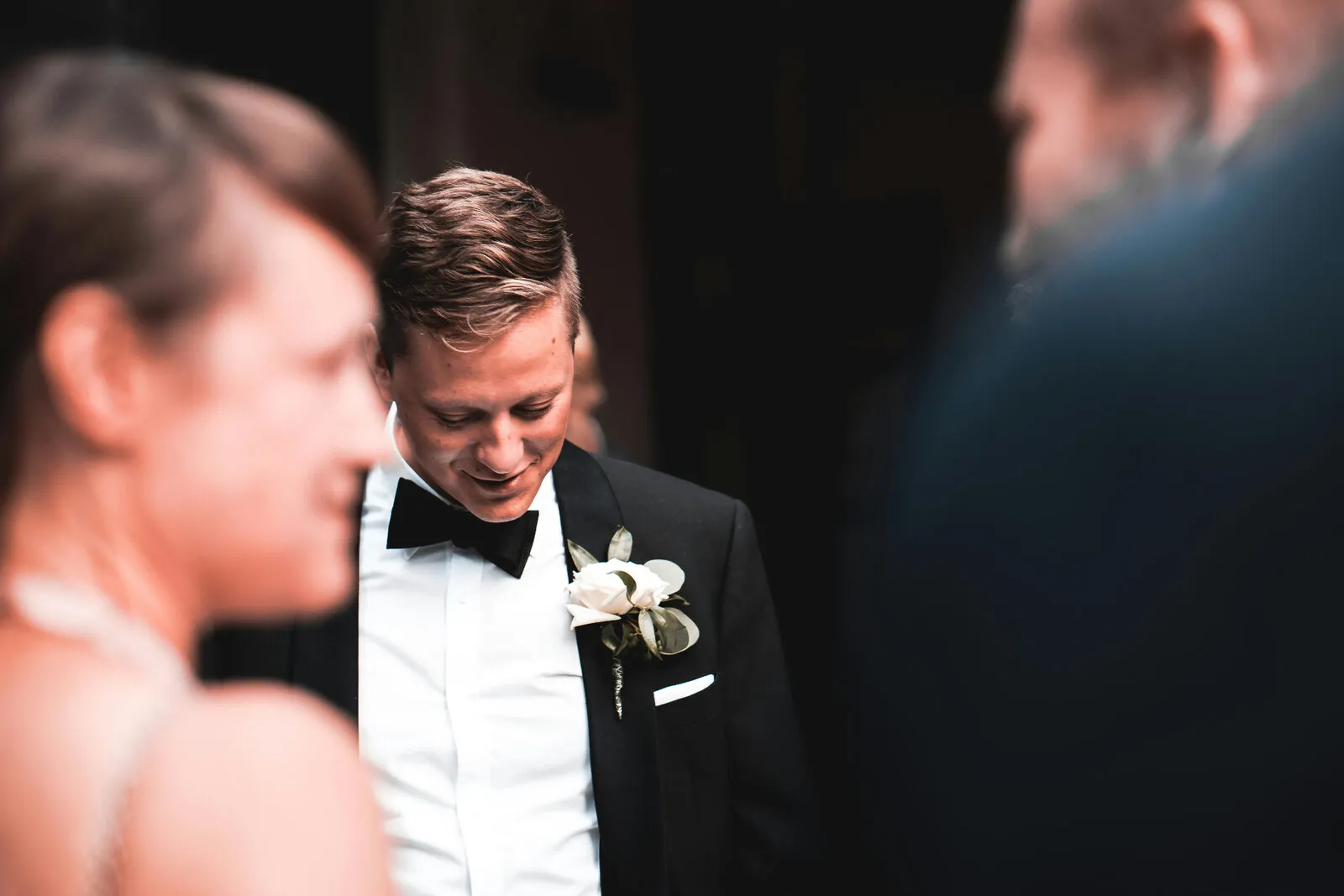Groom in a tuxedo with a white rose boutonnière in a candid moment during the wedding
