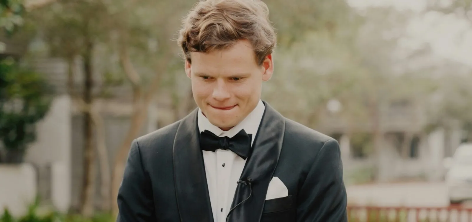 Groom in a black tuxedo and bow tie smiling and looking down before his wedding speech