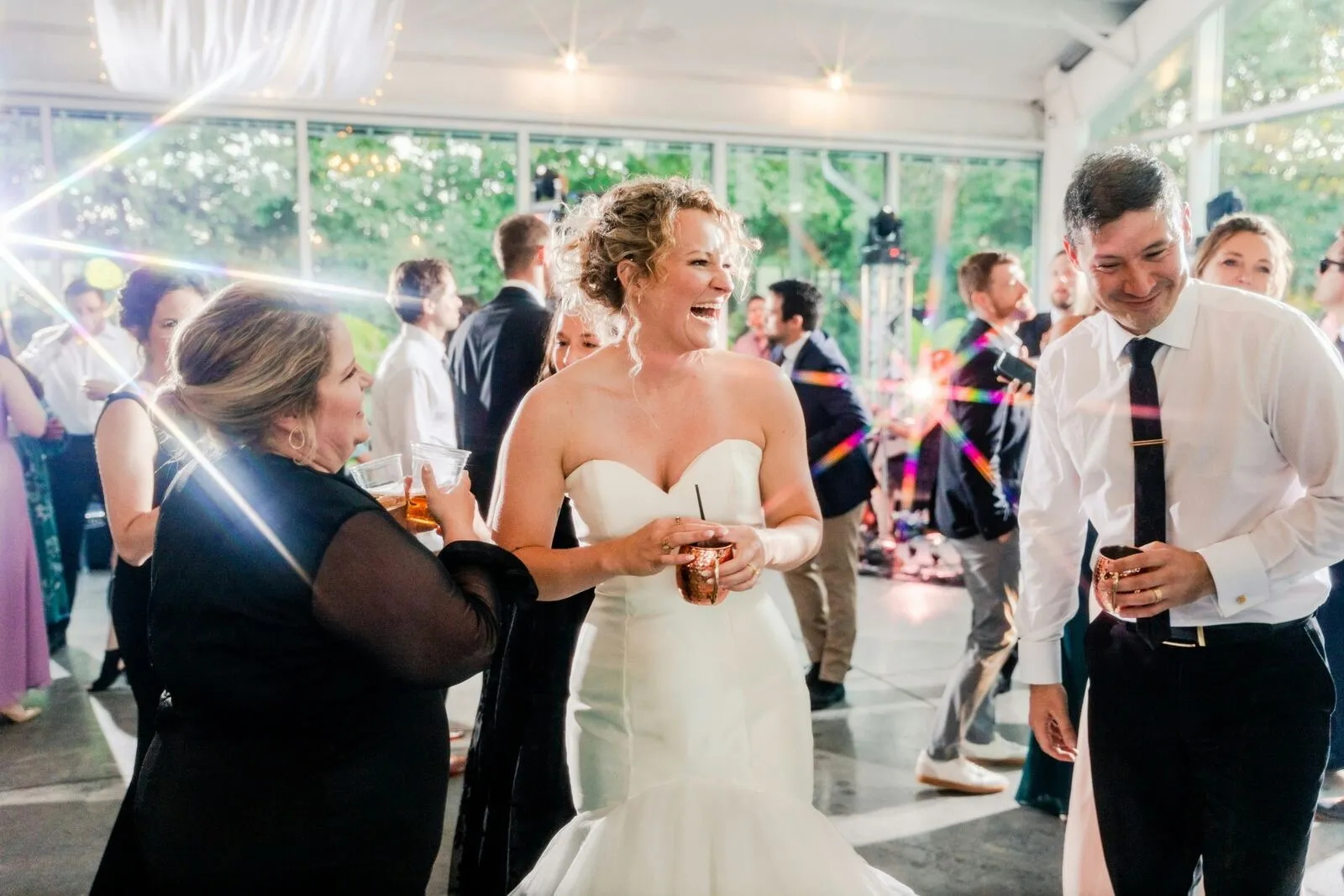Bride laughing and dancing with friends under sparkling reception lights at a wedding party