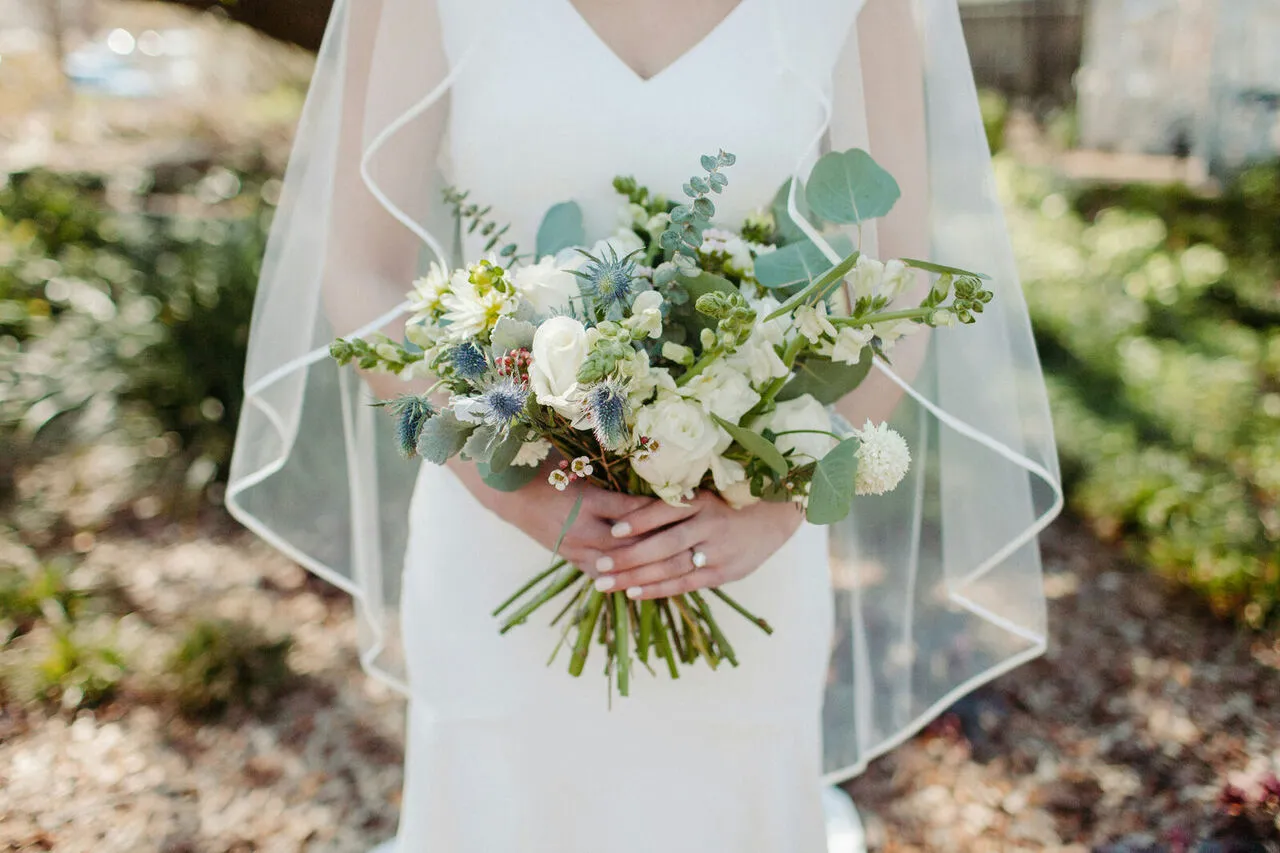 Bride holding a delicate white and eucalyptus bouquet with a soft veil draped behind
