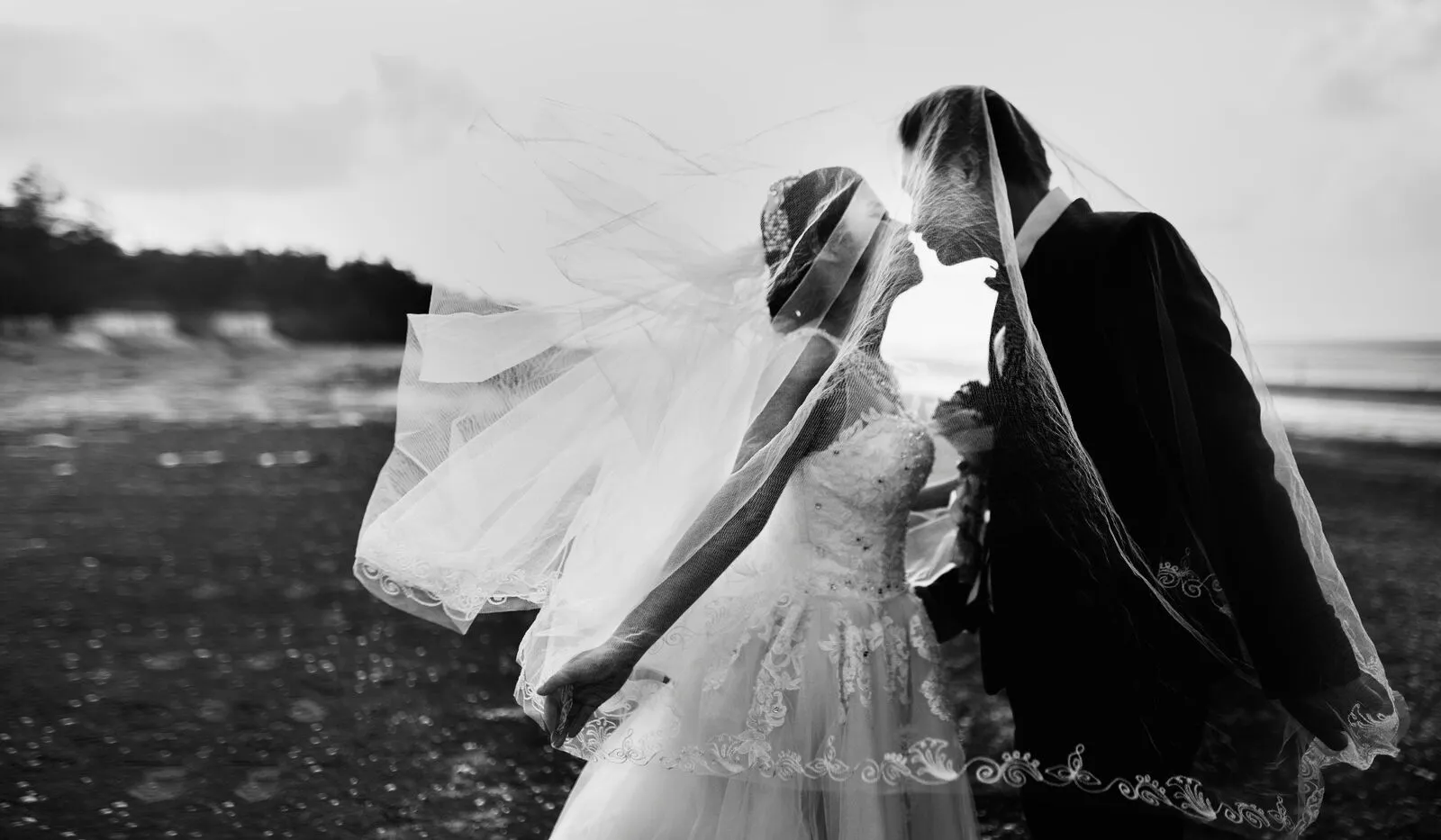 Bride and groom sharing a romantic moment under a flowing veil on the beach