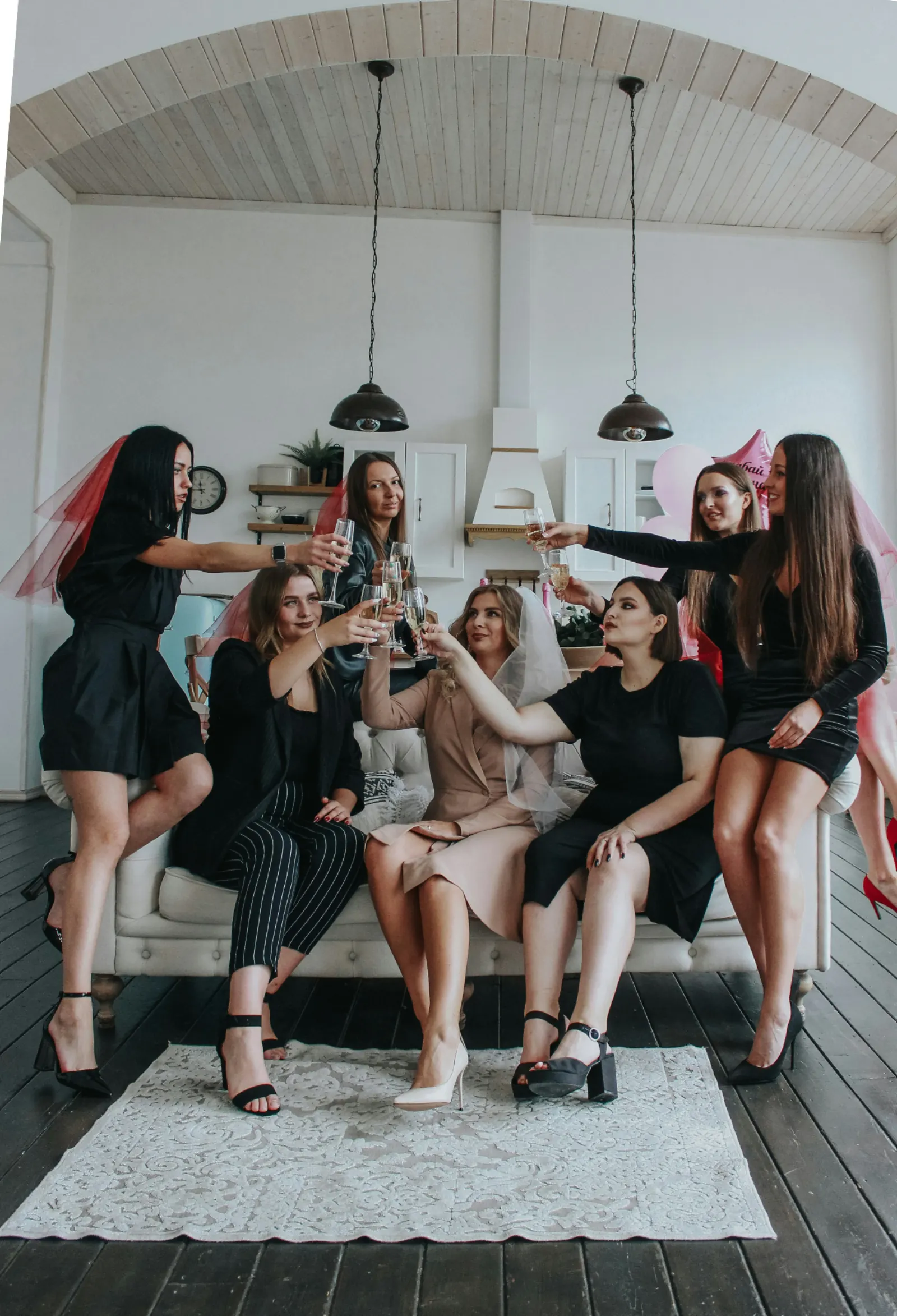 Bride and her bridesmaids in black raising champagne glasses together in a bright sitting room