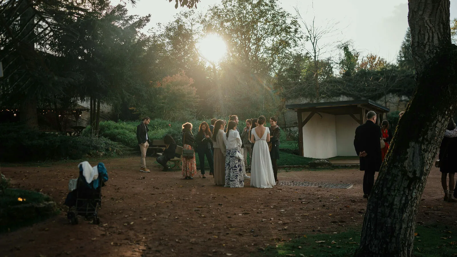 Wedding guests gathered with the bride at sunset in a garden surrounded by tall trees