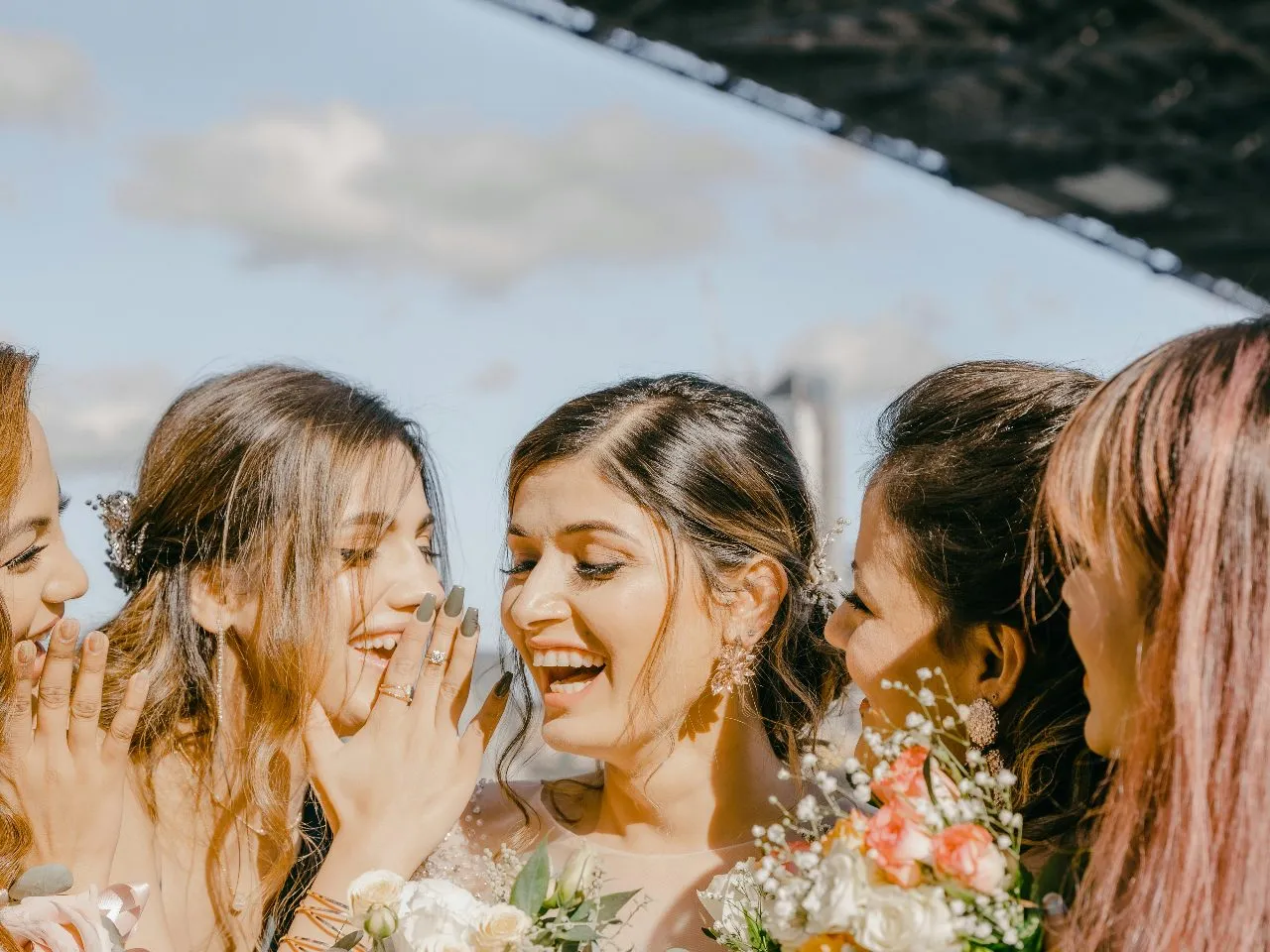 Bride laughing with her bridesmaids and sisters while holding bouquets at her wedding