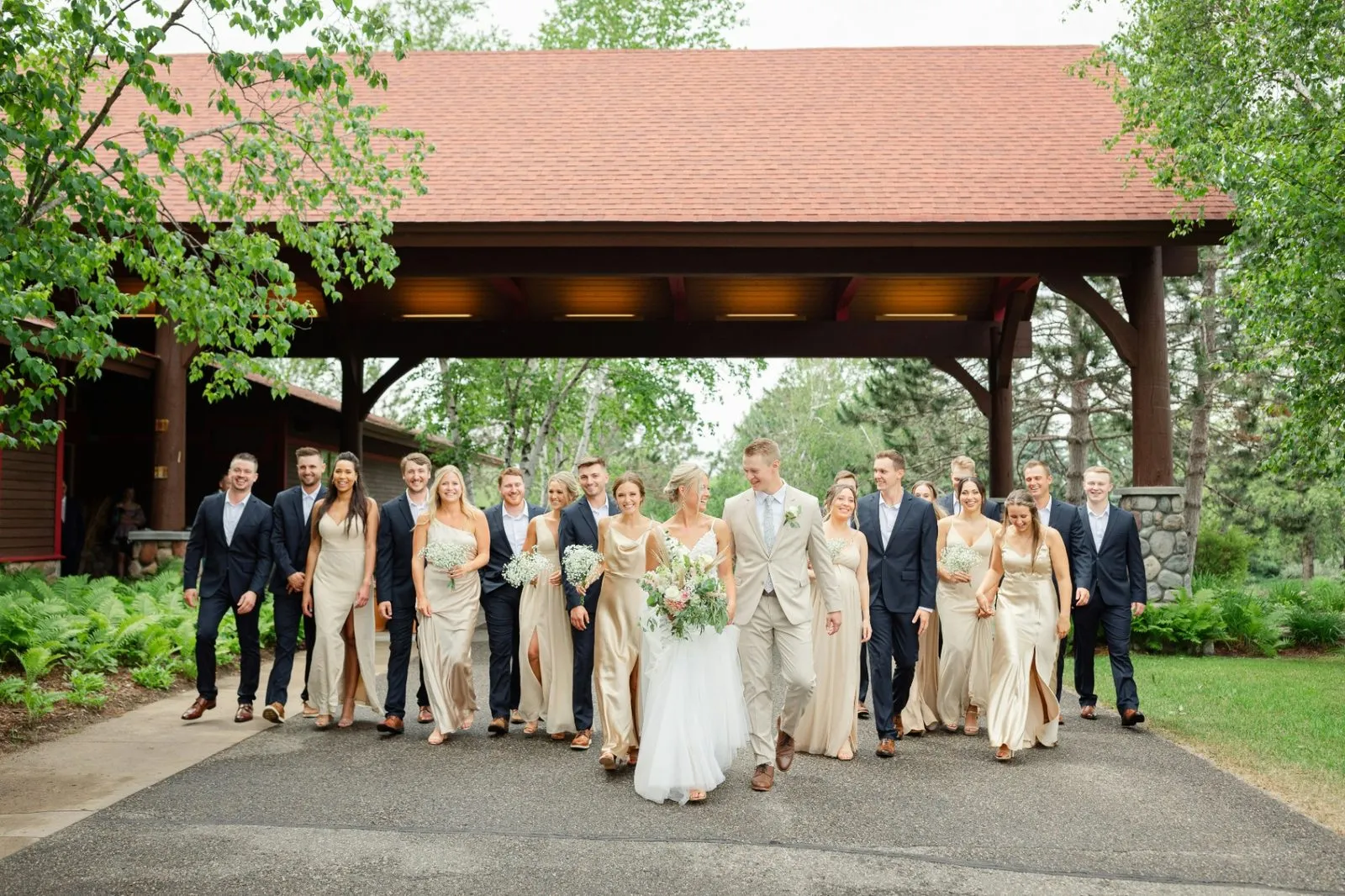 Bride, groom, and full wedding party walking together outside a rustic wedding venue