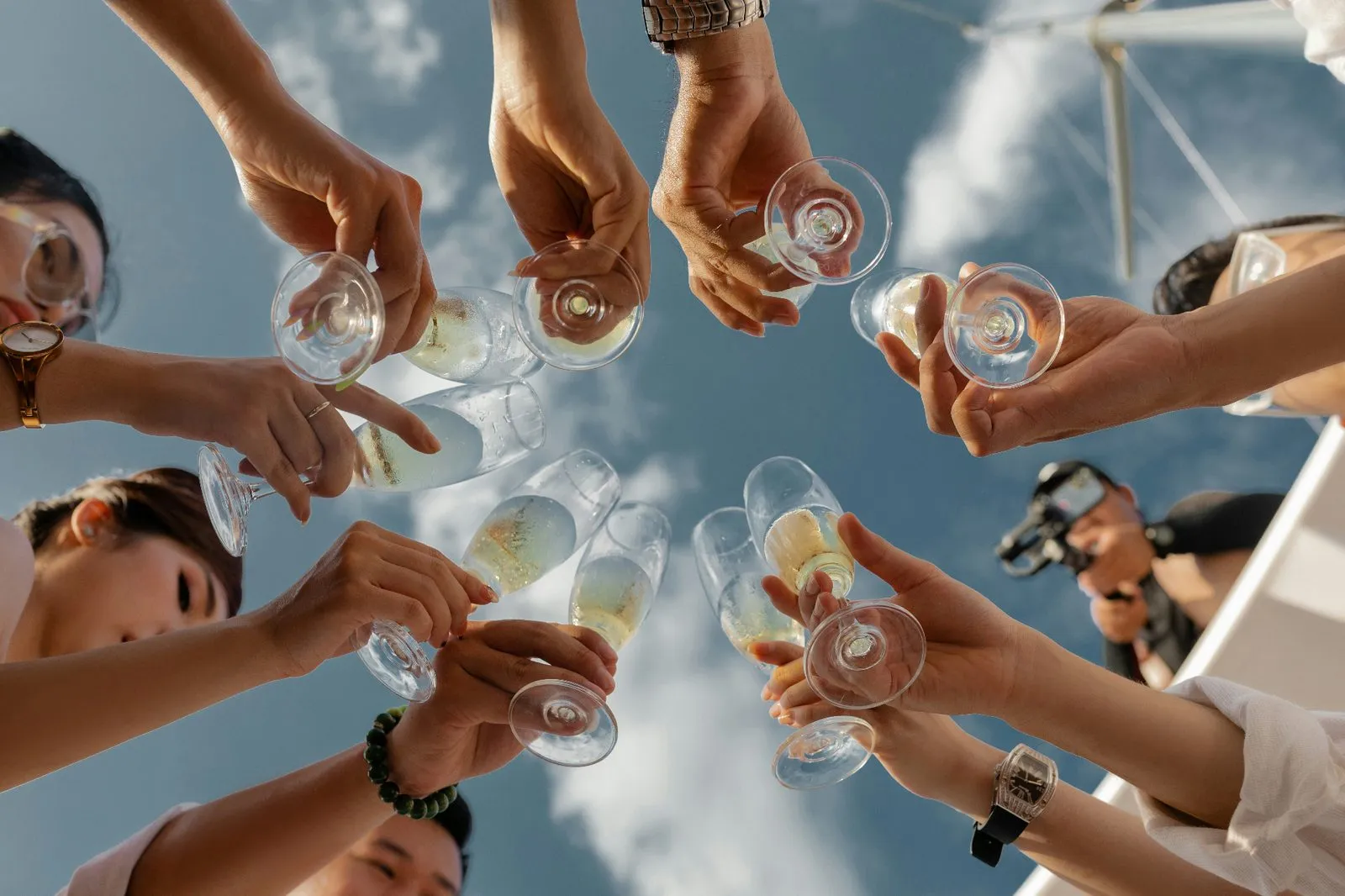 Wedding guests raising champagne glasses in a celebratory toast under a bright sky