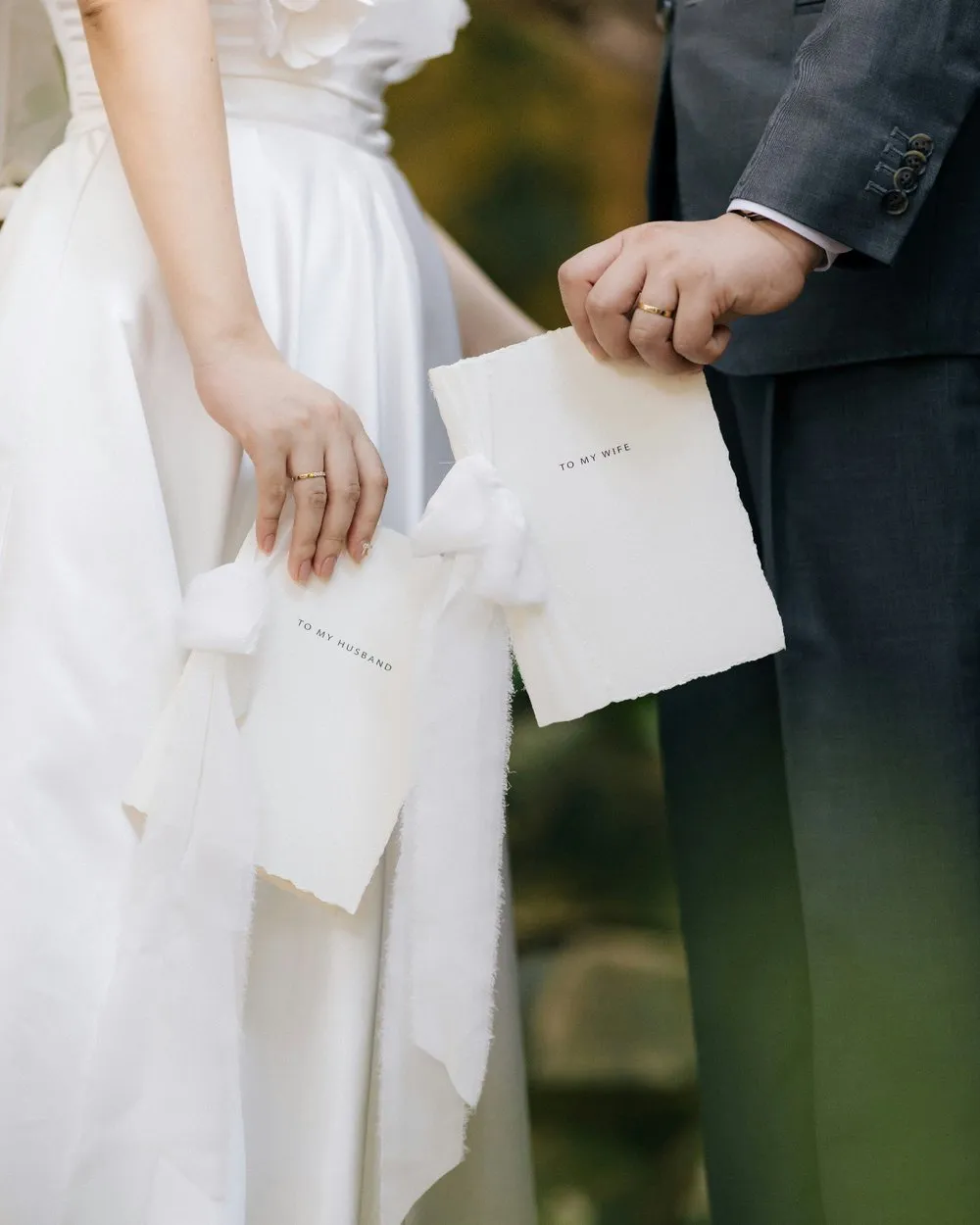 Bride and groom holding hands with two folded handmade vow booklets labeled to my husband and to my wife