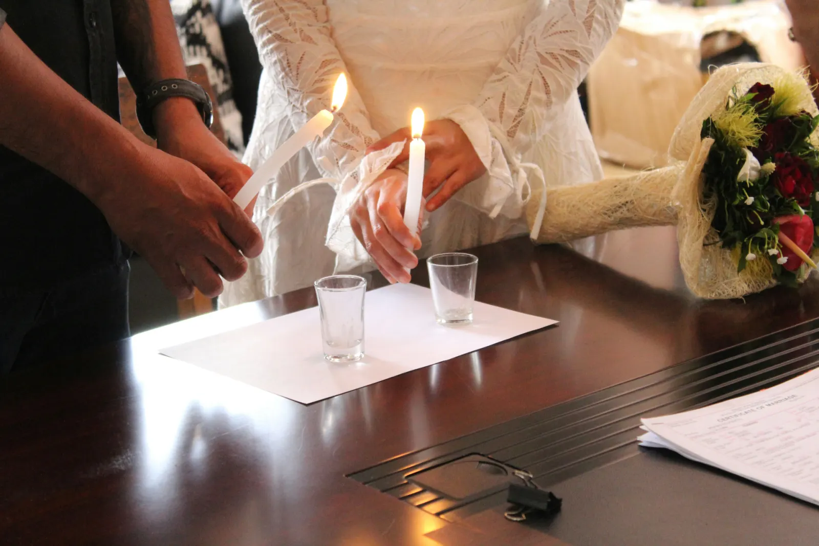 Bride and groom lighting unity candles together on a wooden table during a small ceremony