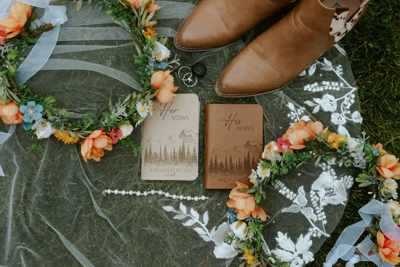 His and Her vow books resting on a soft veil with flowers and boots beside them