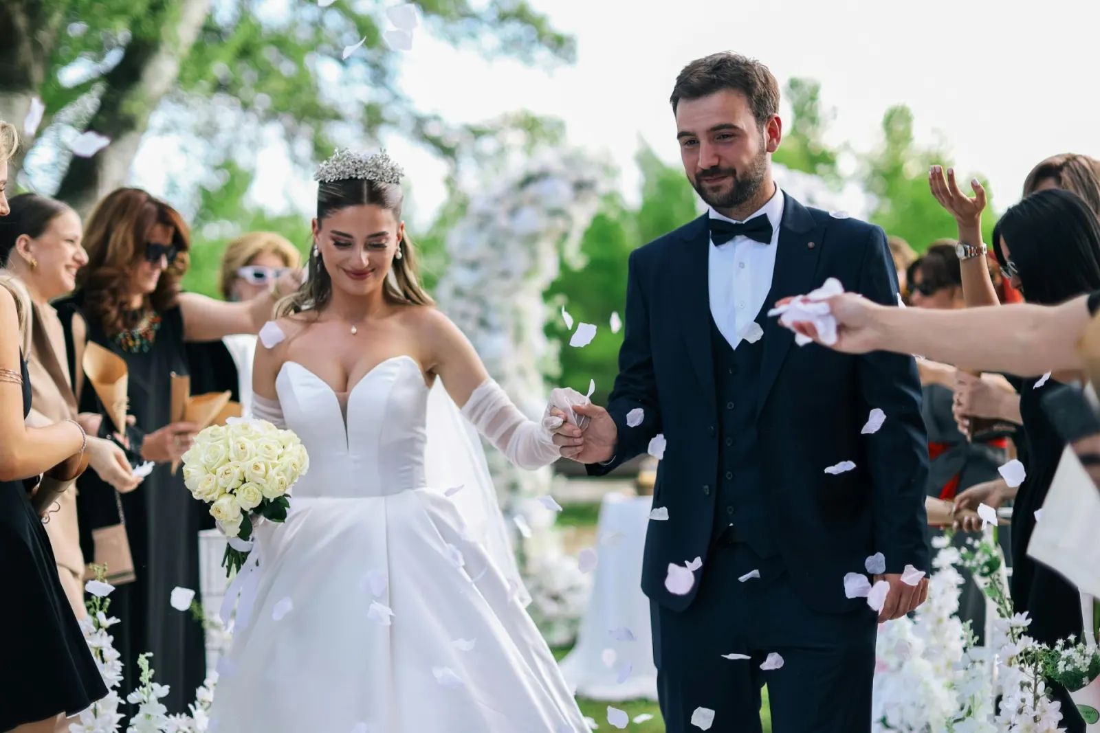 Newlyweds walking back down the aisle hand in hand as guests throw white flower petals