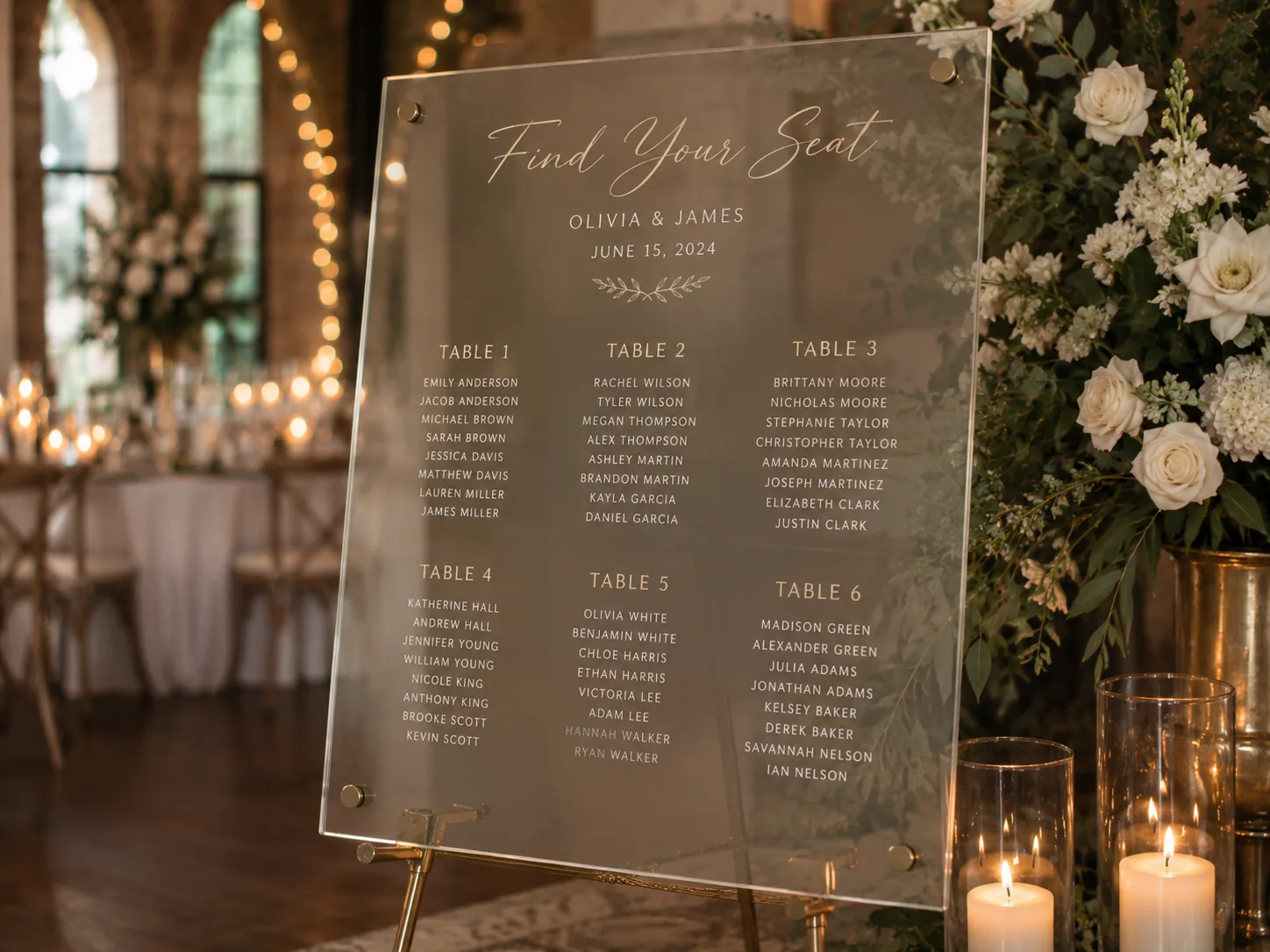 Acrylic Find Your Seat wedding seating chart on a gold easel beside white rose arrangements and candles