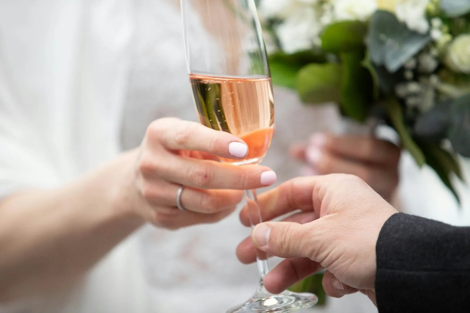 Bride and groom touching champagne flutes in a soft close-up toast with bouquet behind