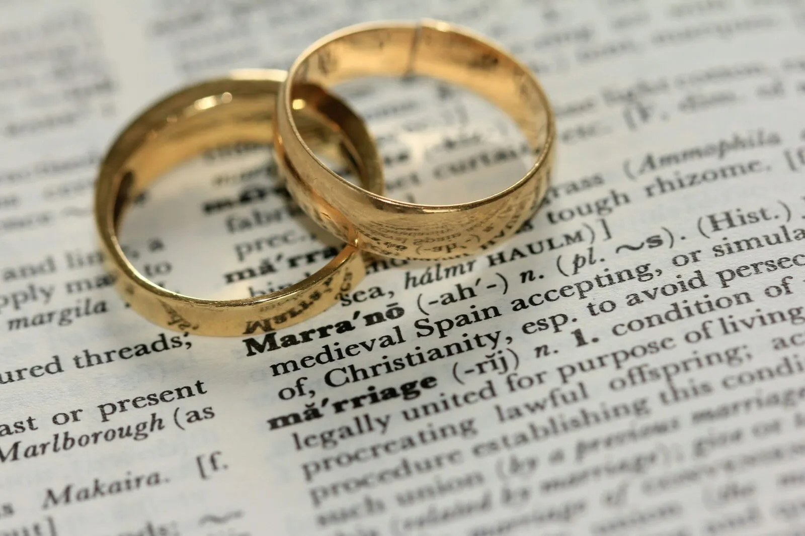 Two gold wedding rings resting on a vintage dictionary page open to the word marriage
